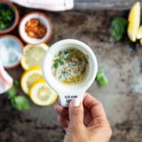 A hand holding a cup of the melted butter sauce to serve with the lobster tail recipe