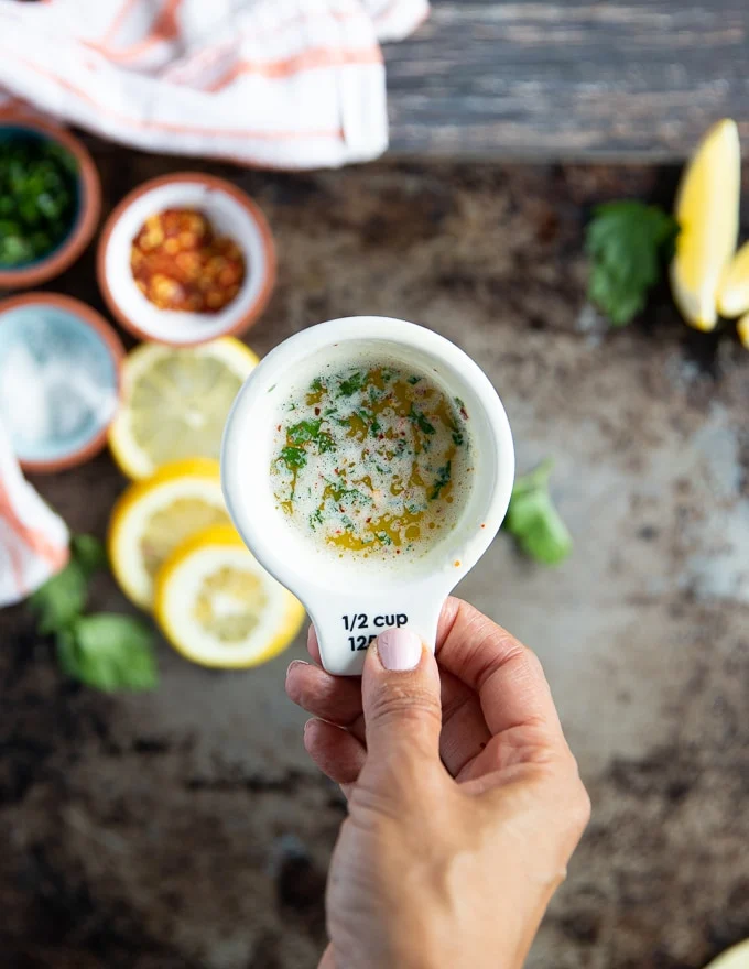 A hand holding a cup of the melted butter sauce to serve with the lobster tail recipe