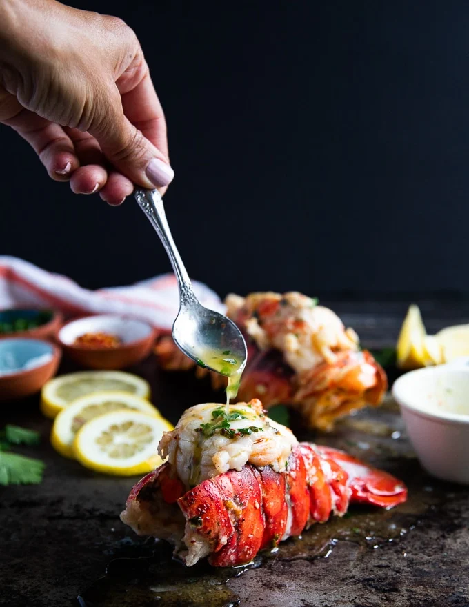 A spoon drizzling some melted butter over the lobster out of the oven