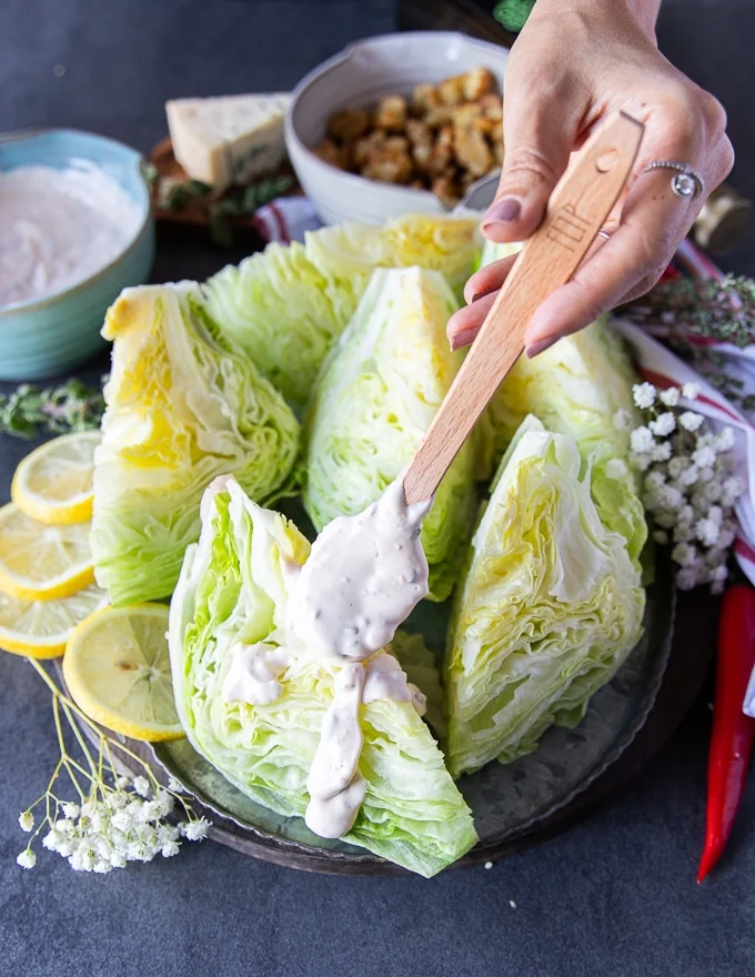 A hand drizzling some blue cheese dressing over ice burg lettuce wedges