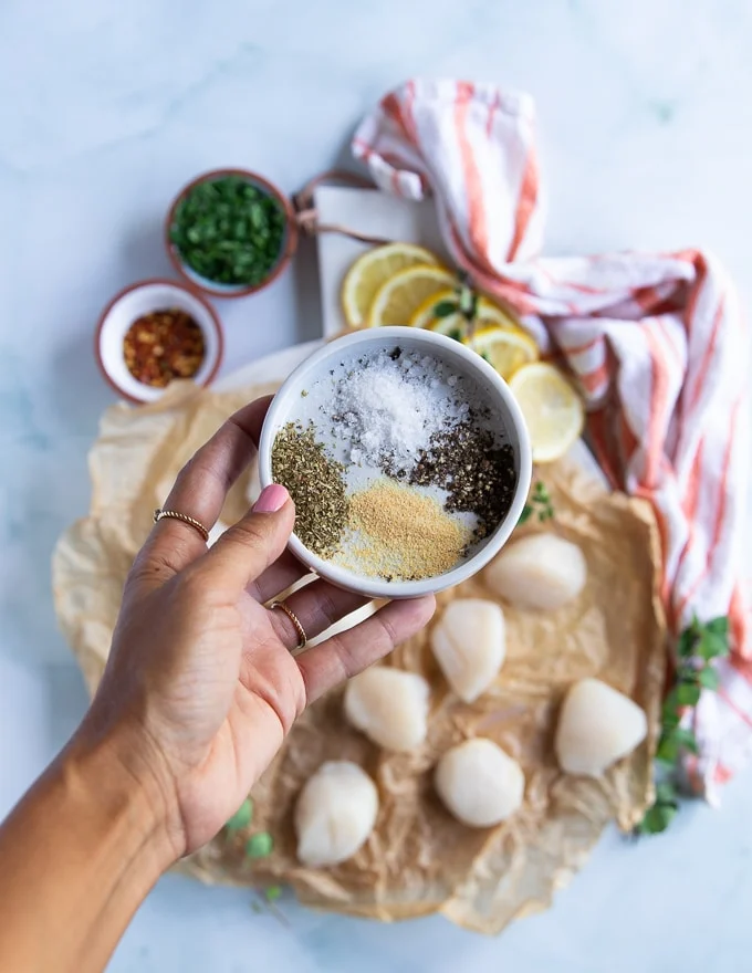A hand holding the spice blend for pan seared scallops including salt, pepper, oregano and garlic powder