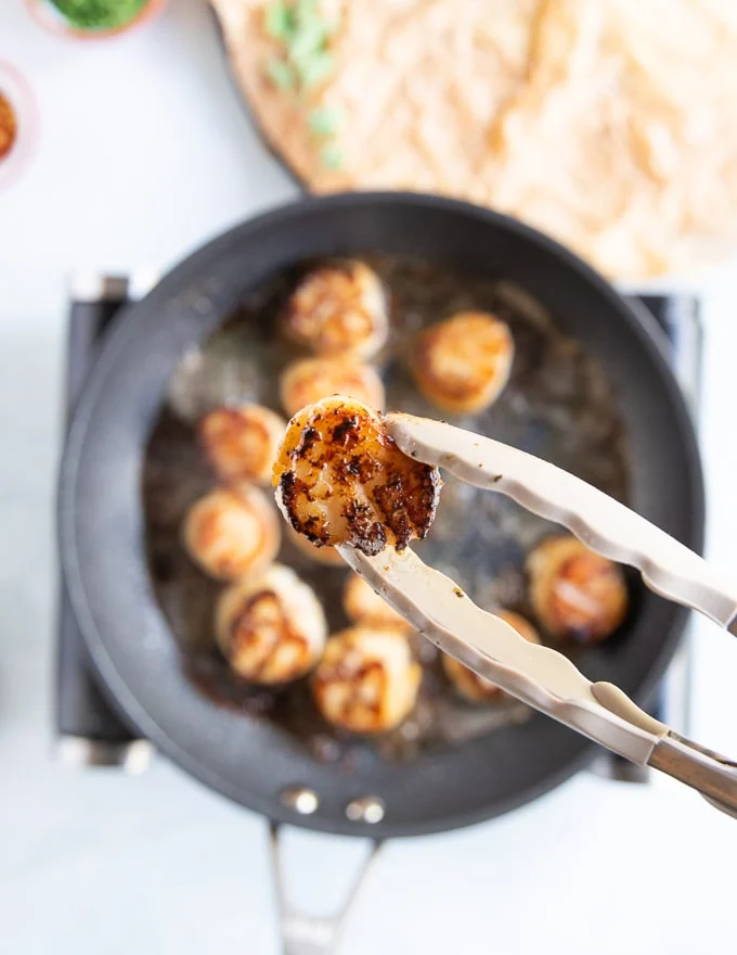 a tong flipping a golden scallop after pan searing