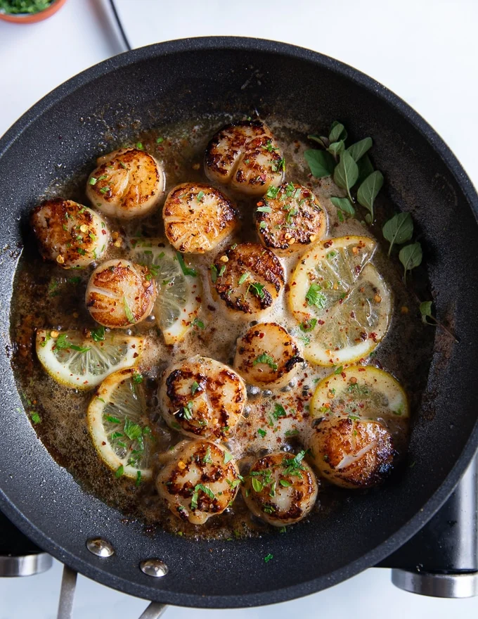 finished pan seared scallops with lemon slices and fresh herbs added in the skillet