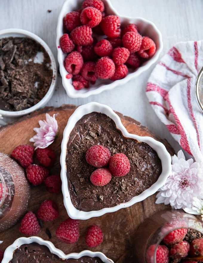 Close-up of finished chocolate pudding recipe in a heart shaped bowl with raspberries and chocolate shavings for garnish.