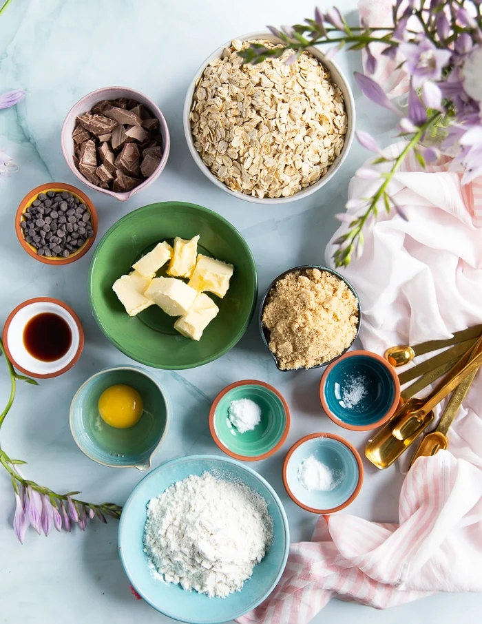 ingredients for oatmeal cookies including butter, oats, sugars, egg, chocolate chips and chunks, flour, salt, baking soda