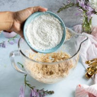 a hand adding in the flour to the oatmeal cookie batter