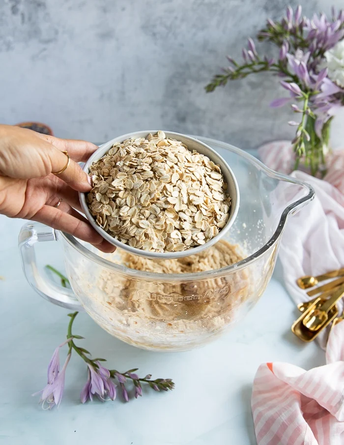 a hand pouring in lots of oats to the bowl of oatmeal cookies