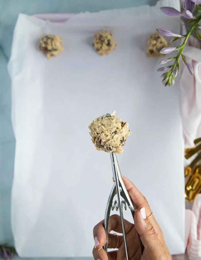 a hand using an ice cream scoop to scoop pieces of cookie dough
