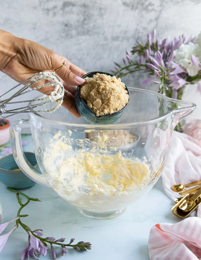 a hand adding in brown sugar to the butter bowl