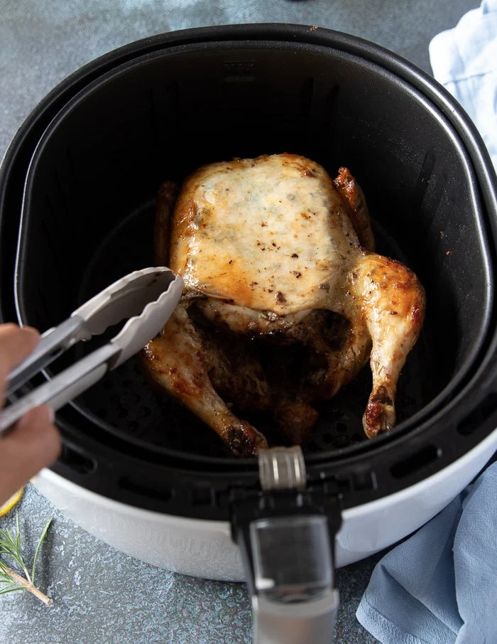 Flipped whole chicken in the air fryer basket with breast side up ready to continue cooking