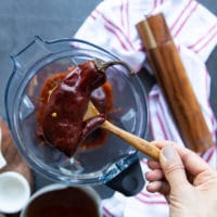 a hand adding in the soaked and ready Guajillo chillies into the blender for the sauce