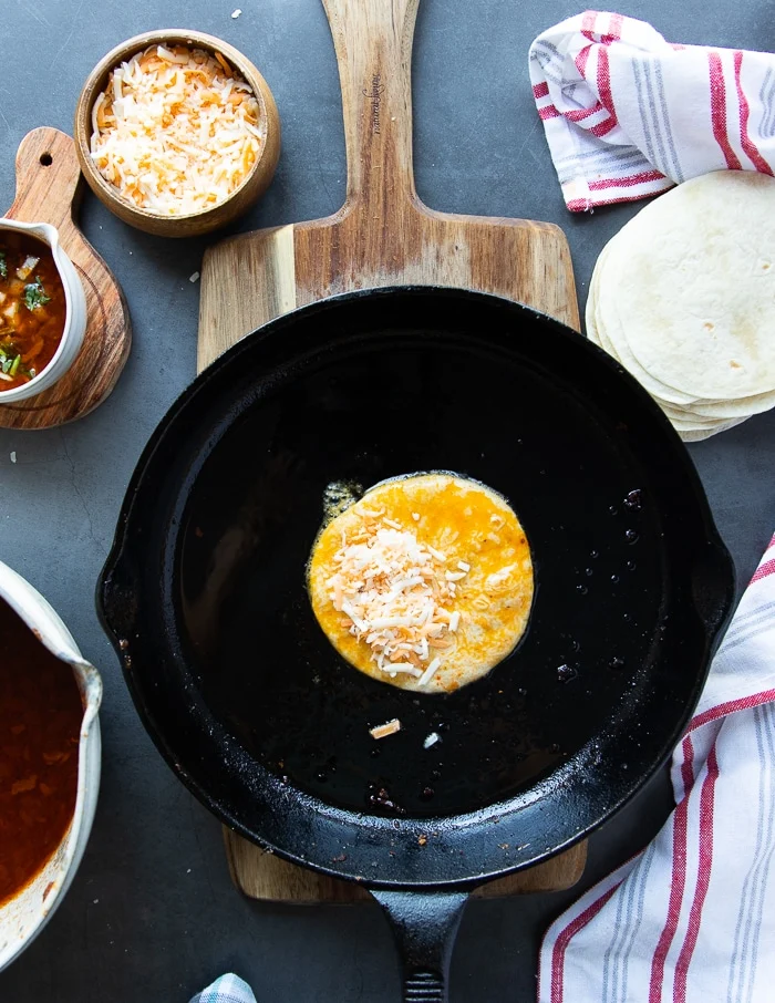 the dipped tortilla in a pan with cheese placed on one half of it