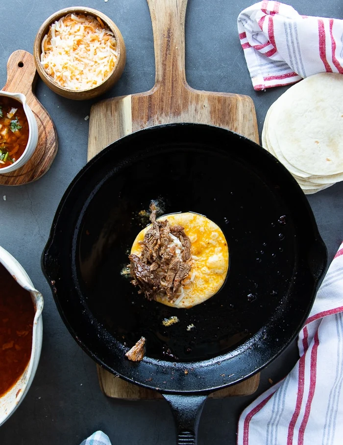 the birria meat is added over the cheese on the tortilla
