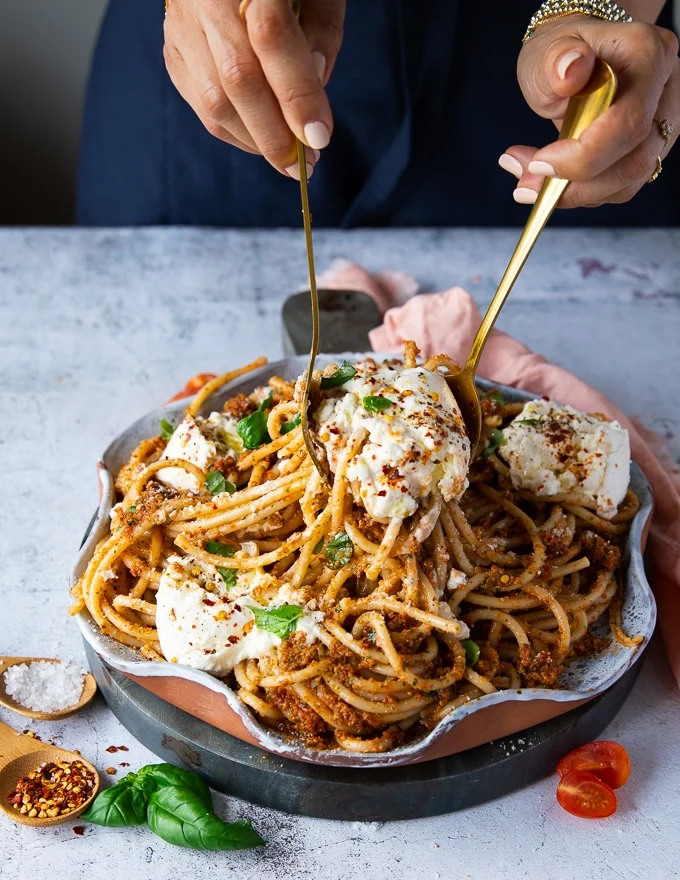 two spoons serving and tossing the burrata pasta and serving it.