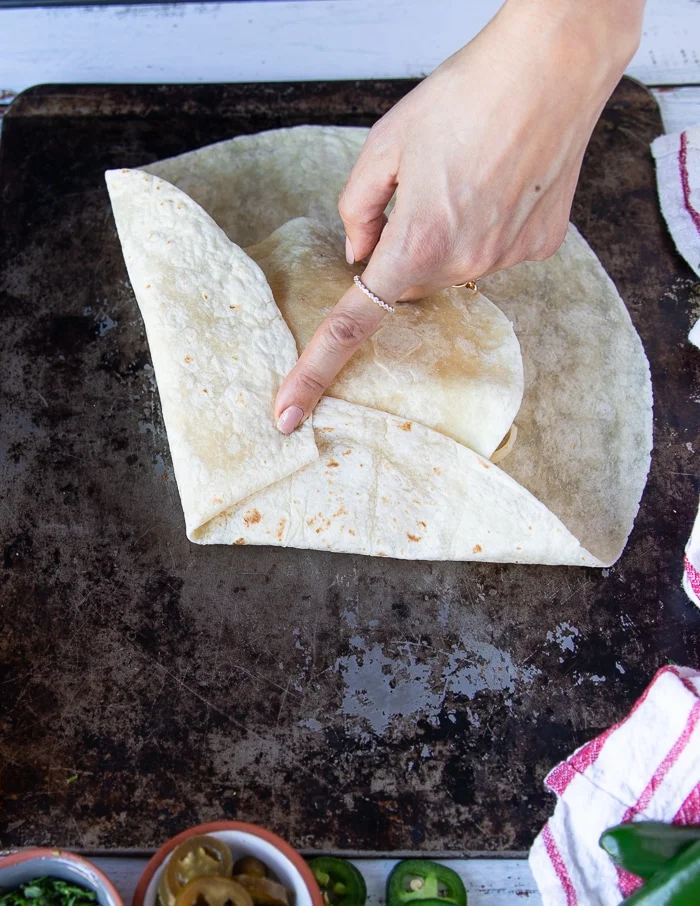 process of folding the crunchywrap supreme with one hand holding firm one part of the tortilla and the other side being folded over