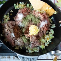 all meat ingredients added to the pan including ground beef or lamb, minced garlic, spices and seasoning