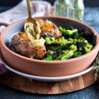 A spoon spreading in some roast garlic butter over the air fried chicken breasts on the serving plate and ready to serve