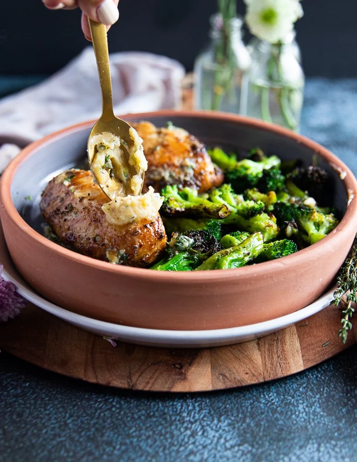 A spoon spreading in some roast garlic butter over the air fried chicken breasts on the serving plate and ready to serve