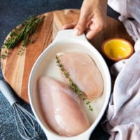 chicken breasts are placed in a bowl with the brine and a sprig of fresh thyme before air frying the4 chicken breasts