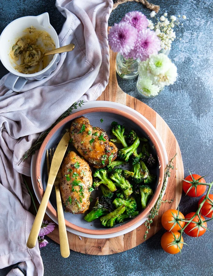 two air fried chicken breasts on a serving olate with some air fried broccoli and a fork and knife for serving on the side.