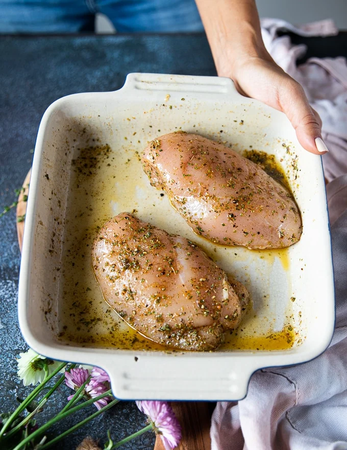 The chicken breasts placed in a plate all sprinkled with seasoning and olive oil