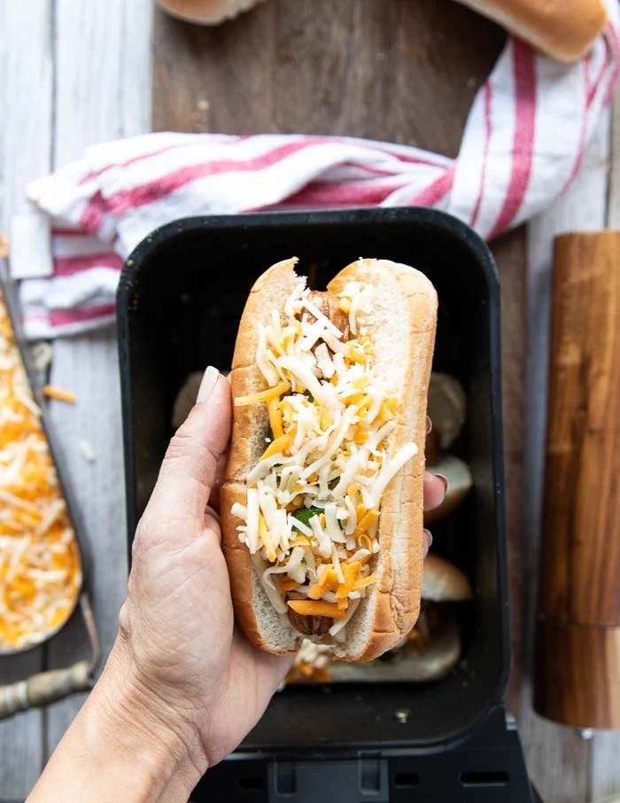 adding shredded cheese over the hot dog in the bun