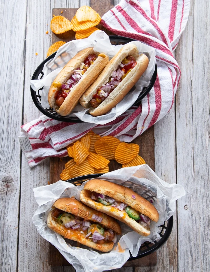 two plates of air fryer hot dogs all dressed up differently showing the variety of hot dog toppings