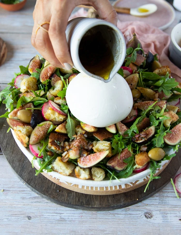 A hand pouring the balsamic salad dressing over the burrata cheese salad
