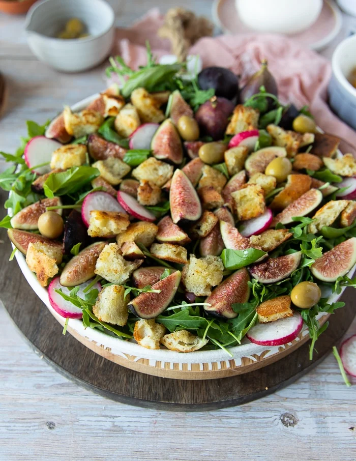 Remaining burrata salad ingredients are added to the salad plate including radishes, croutons, olives