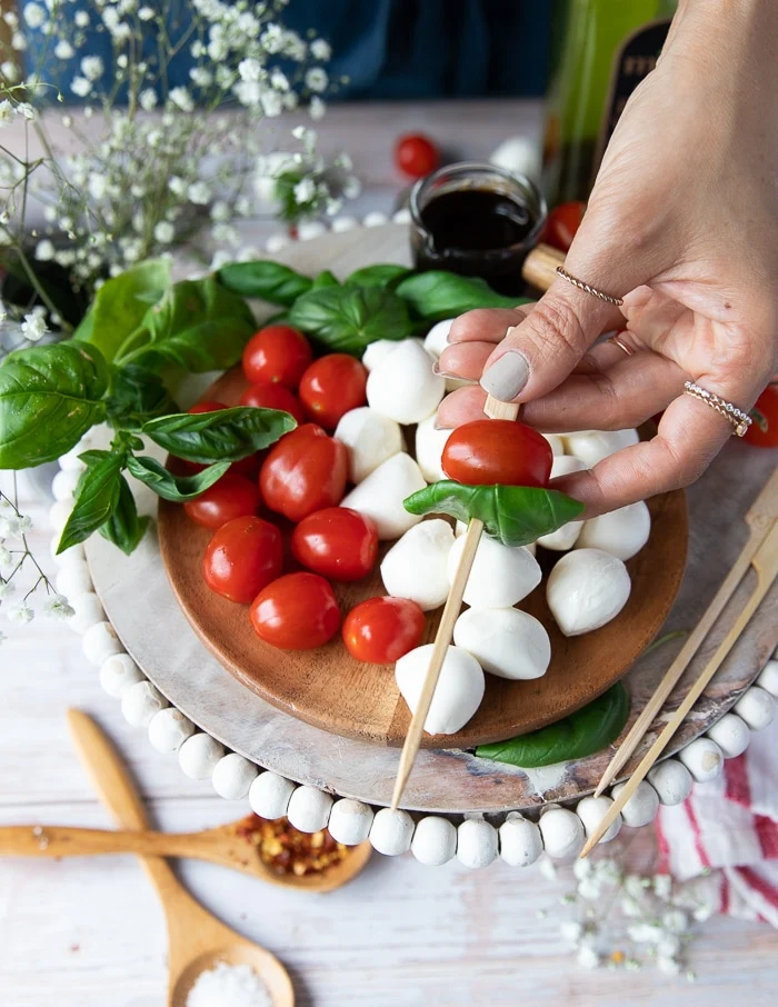A hand holding a wooden skewer skewering a tomato