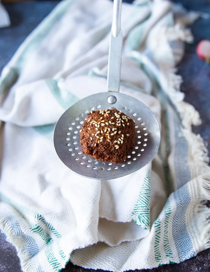 ladle holding up a fried falafel showing the golden crust