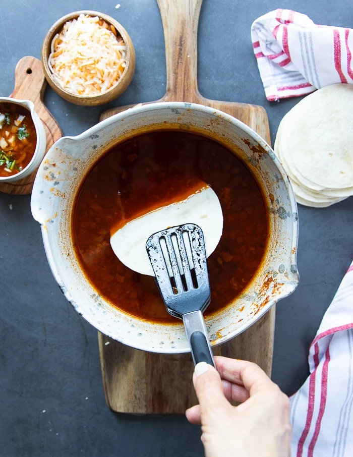 the tortillas are being dipped into the birria stew sauce before searing