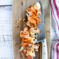 A cut up lobster tail on a wooden board with a knife next to it