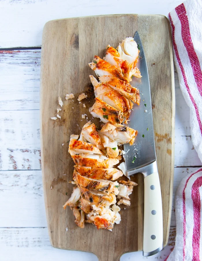 A cut up lobster tail on a wooden board with a knife next to it