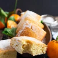 A piece of bitten up mandarin orange cake on a wooden board