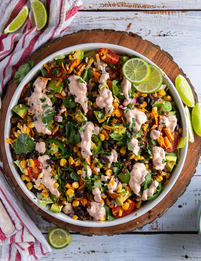 top view of a large plate of taco salad with creamy dressing surrounded by lime wedges