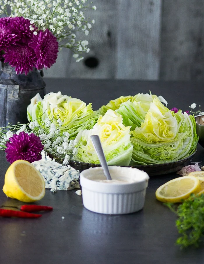 A bowl of blue cheese dressing placed next to cut up iceberg wedges