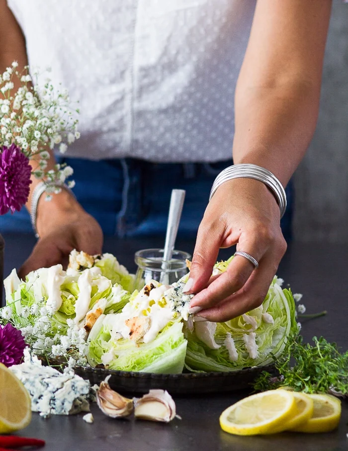 A hand adding crumbles of blue cheese over the wedge salad