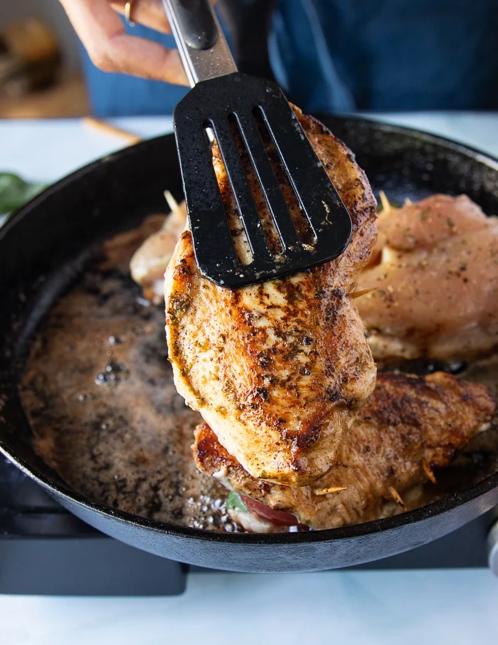A tong flipping one side of the caprese chicken to show the golden crust