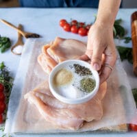 a hand holding a bowl of chicken seasoning to sprinkle on the inside and outside of the chicken