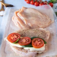 A chicken breast with layers of mozzarella cheese, tomatoes and lots of fresh basil leaves on top