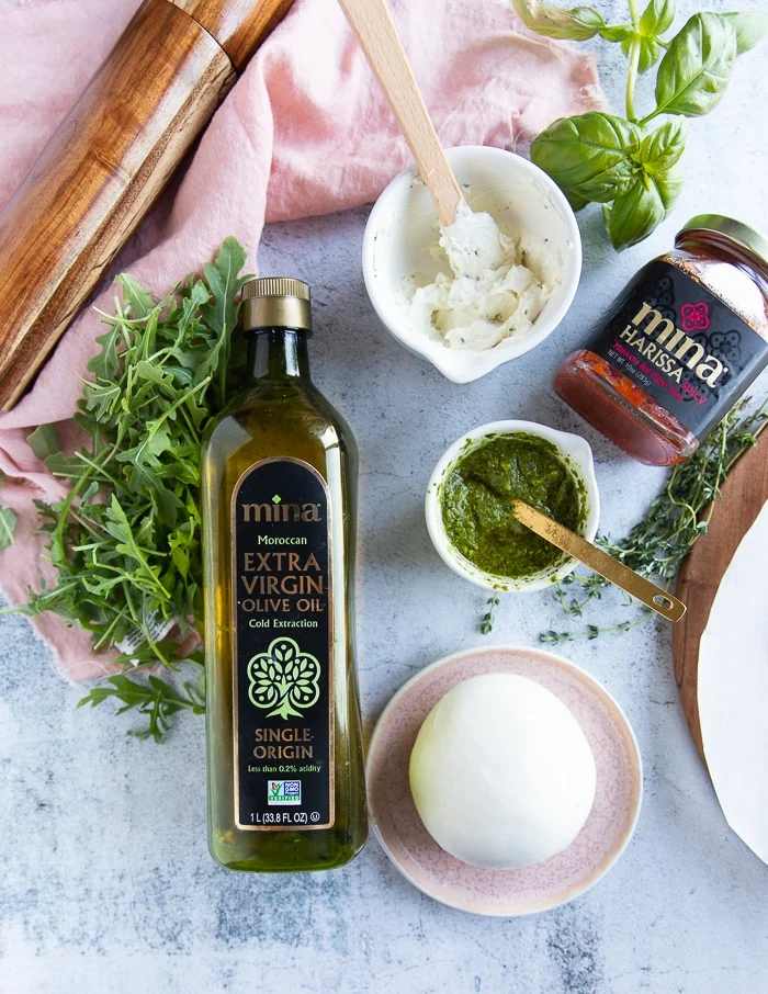 Burrata Pizza Ingredients: white sauce, olive oil, pesto, harissa, pizza dough, arugula.