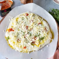 Uncooked pizza ready for the oven covered in mozzarella and drizzled with harissa sauce.