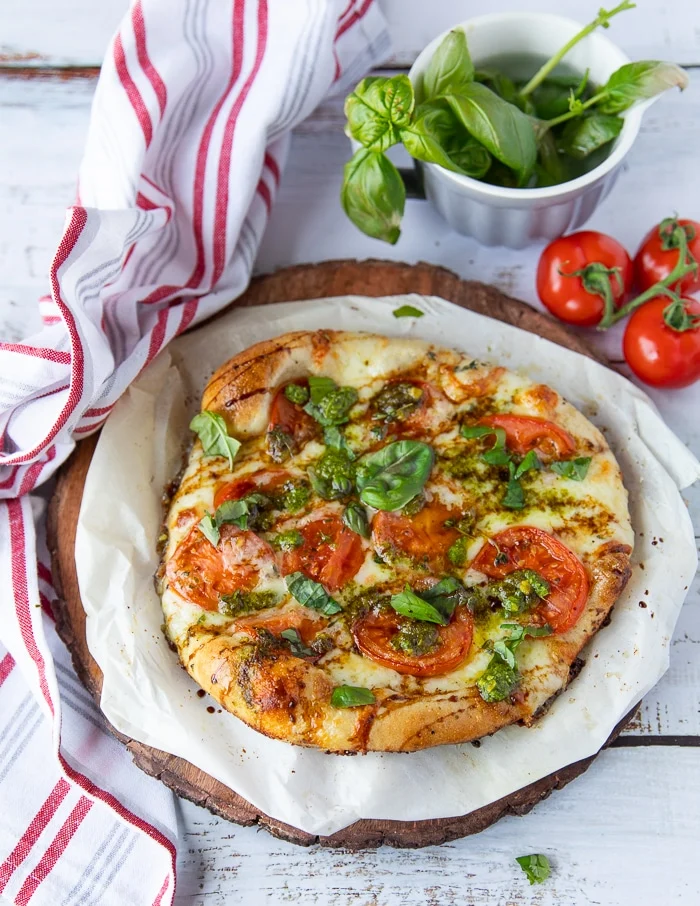 A caprese pizza out of the oven with balsamic drizzle and more fresh basil leaves