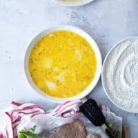 breading station for veal parmesan recipe including a plate of seasoned flour, plate of seasoned eggs, plate of seasoned breadcrumbs