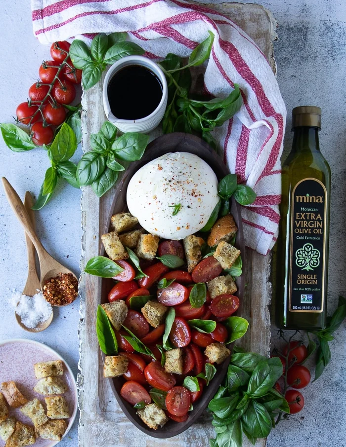a large plate of burrata caprese surrounded by quality olive oil, more salt and chilli flakes, some basil leaves and extra balsamic