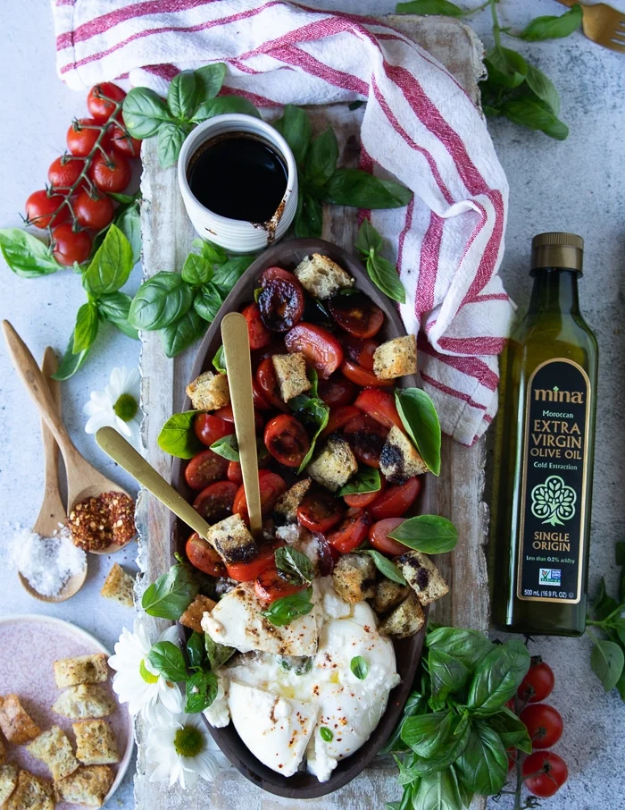 two spoons breaking up a burrata cheese in the burrata caprese plate