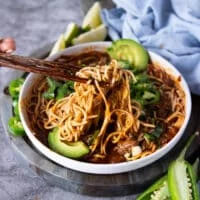 two chopsticks stretching out the birria ramen showing the rich birria stew and birria meat drenching the noodles with al the toppings