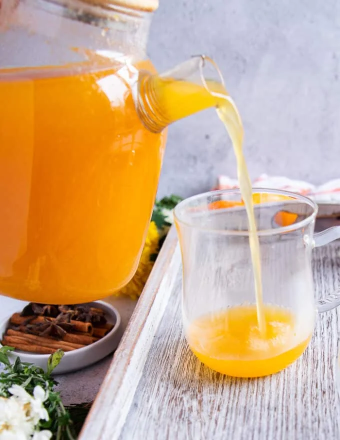 A glass jar pouring fresh homemade apple cider into a class cup