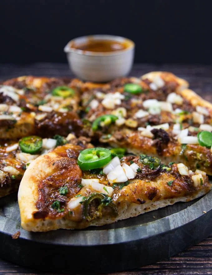 one close up slice of birria pizza showing the texture of the dough, the toppings, the cheese, the meat and the birria stew for dipping